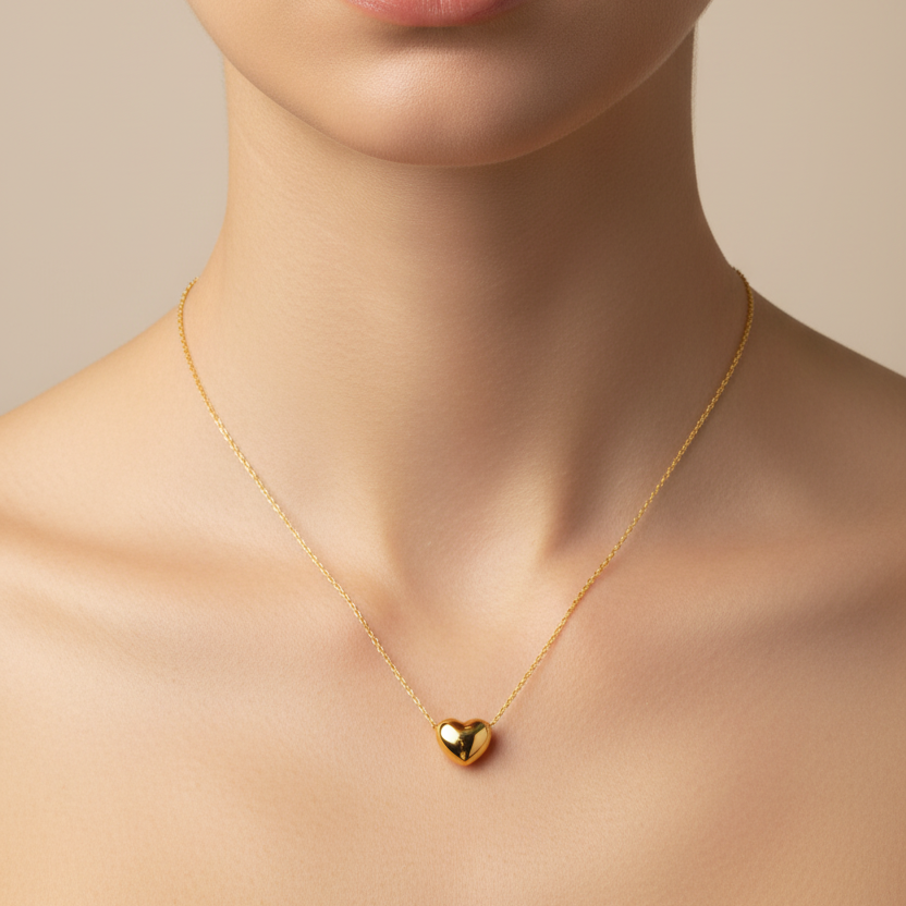 A close-up of a Gold Mini Heart Necklace, worn on the neck of a model against a soft beige background.