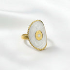 Gold Oval Statement Ring  with a white stone on a beige fabric background