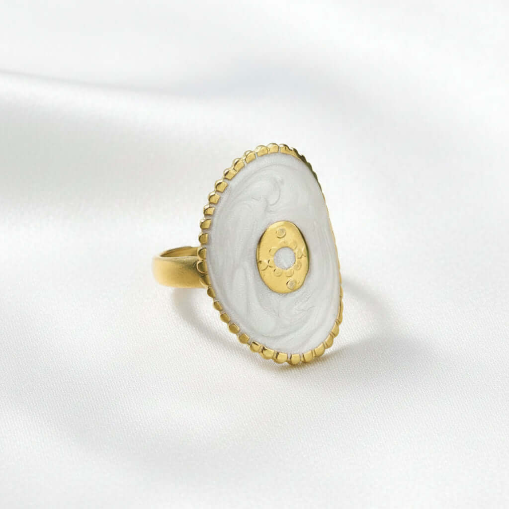 Gold Oval Statement Ring  with a white stone on a beige fabric background