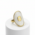 Gold Oval Statement Ring with a stone on a white cylindrical stand against a white background