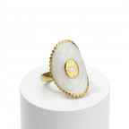 Gold Oval Statement Ring with a stone on a white cylindrical stand against a white background
