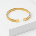 Gold Ribbed Coil Bangle Bracelet on white square pedestal
