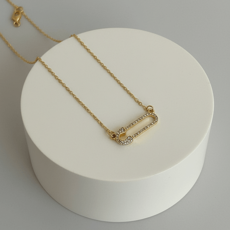 Gold Safety Pin Pendant Necklace with a white round base on a light gray background