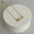 Gold Safety Pin Pendant Necklace with a white round base on a light gray background