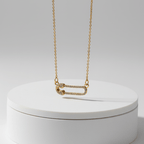 Gold Safety Pin Pendant Necklace on a white round box against a light gray background