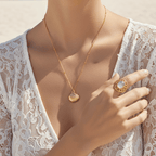Woman wearing Gold Scallop Shell Pendant Necklace and ring on a beach