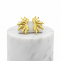 A pair of Gold Sculpted Petal Stud Earrings displayed on a white rectangular block atop a white marble cylinder against a white background.