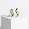 A pair of Gold & Silver Intertwined Stud Earrings, displayed on a white geometric pedestal against a clean white background.