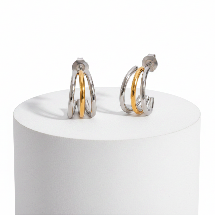 A pair of silver hoop earrings with a single gold accent band, displayed on a white cylindrical pedestal against a white background.