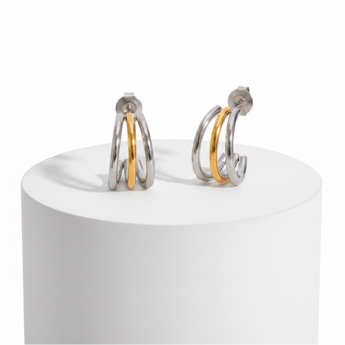A pair of silver hoop earrings with a single gold accent band, displayed on a white cylindrical pedestal against a white background.