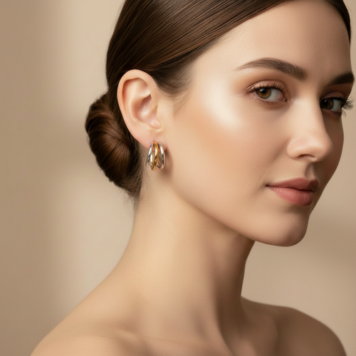 A close-up portrait of a woman wearing a pair of Gold & Silver Layered Hoop Stud Earrings with layered curved bands, set against a soft beige background.