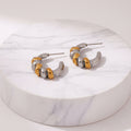 A pair of silver and gold hoop earrings with a textured, segmented design, shown on a light off-white background with dimension and weight labels.