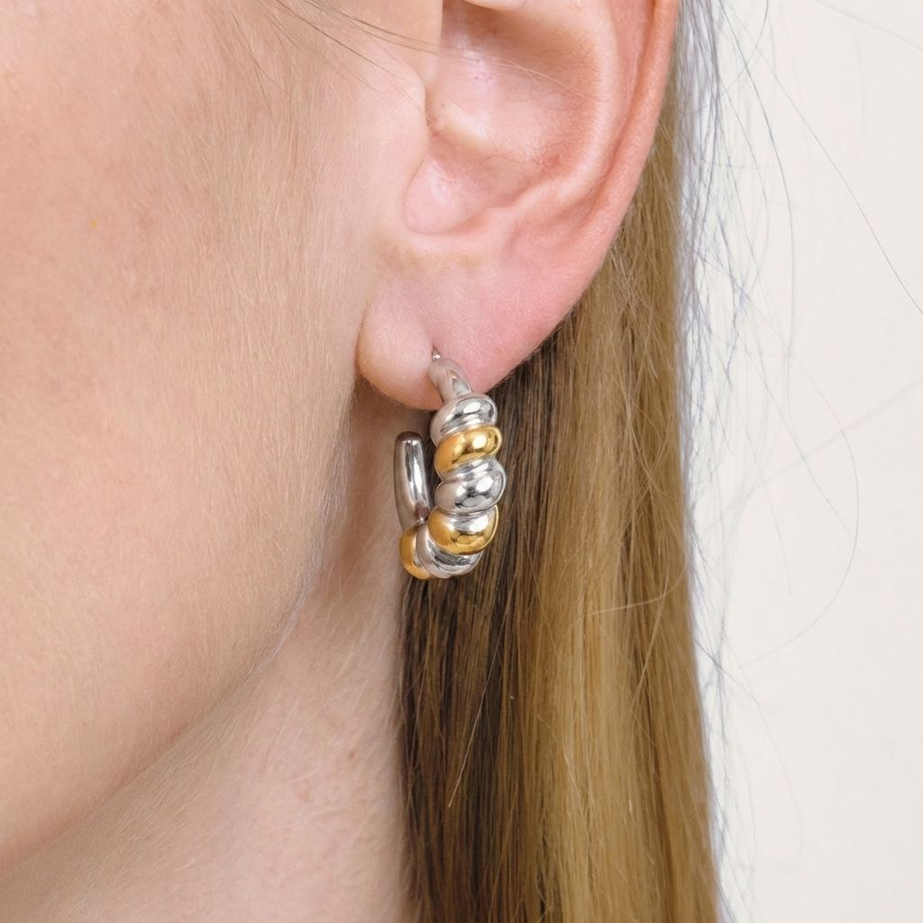 A close-up of a person's ear wearing a Gold & Silver Segmented Hoop Earrings, against a light neutral background.