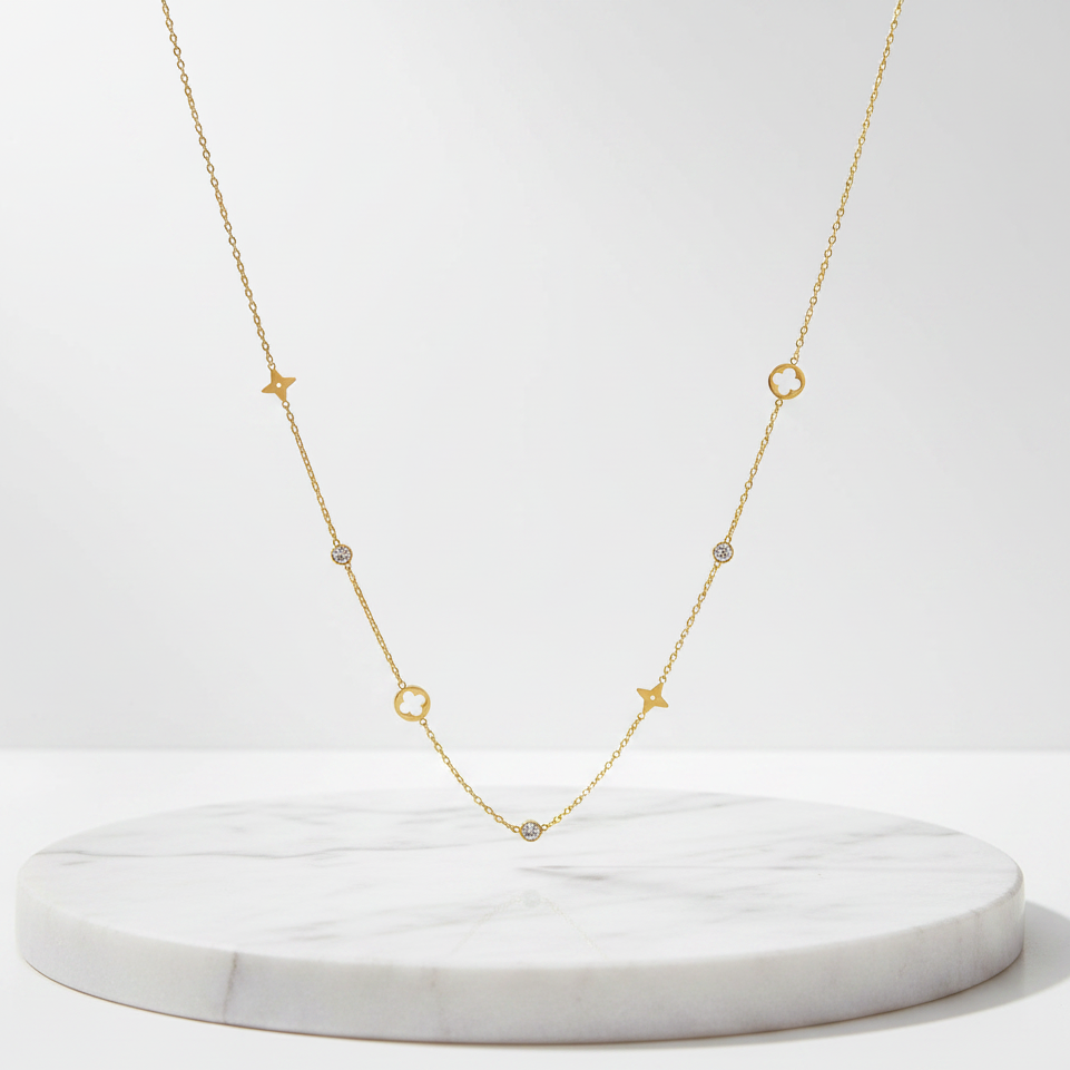 A delicate Gold Star & Clover Charm Necklace, displayed on a round white marble pedestal against a clean white background.