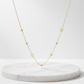 A delicate Gold Star & Clover Charm Necklace, displayed on a round white marble pedestal against a clean white background.