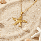 Gold Starfish Pendant Necklace on a sandy surface with seashells and starfish.
