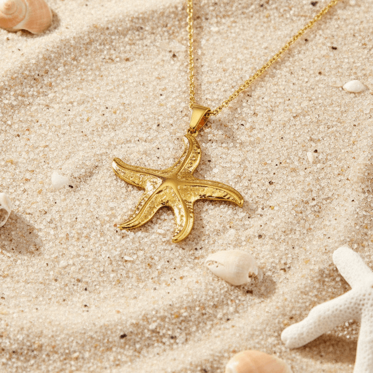 Gold Starfish Pendant Necklace on a sandy surface with seashells and starfish.