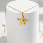 Gold Starfish Pendant Necklace on a white stand with a blurred background
