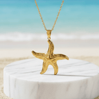 Gold Starfish Pendant Necklace on a white marble stand with a beach background