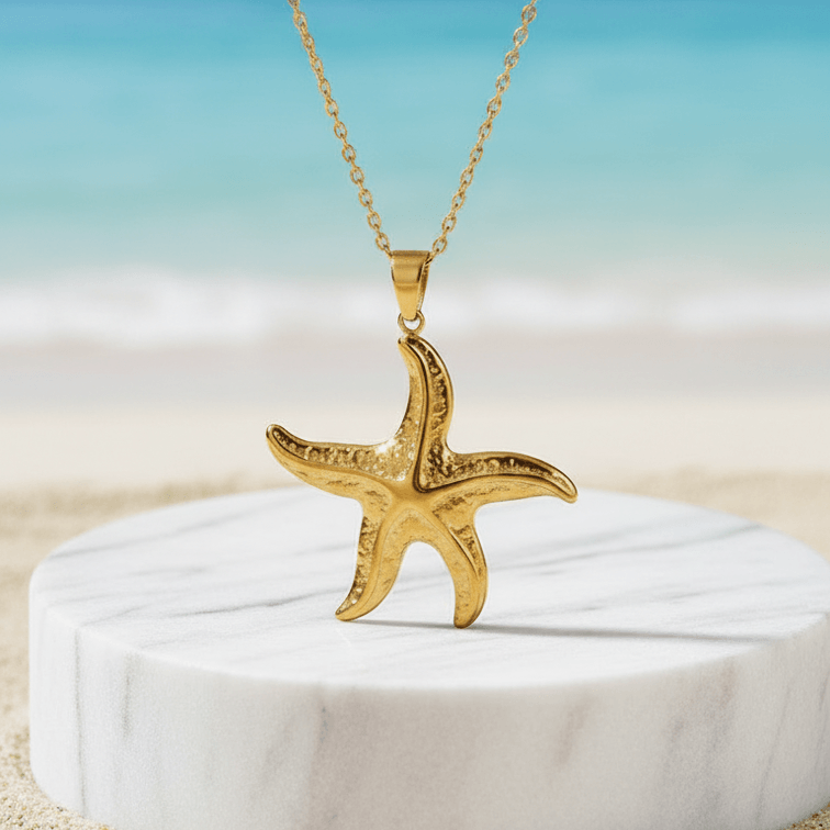 Gold Starfish Pendant Necklace on a white marble stand with a beach background