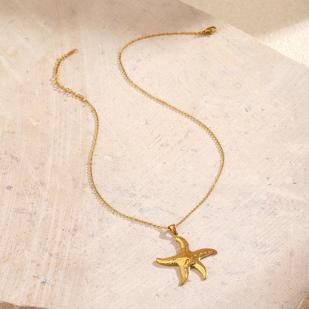 Gold Starfish Pendant Necklace on a textured beige surface