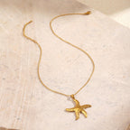 Gold Starfish Pendant Necklace on a textured beige surface