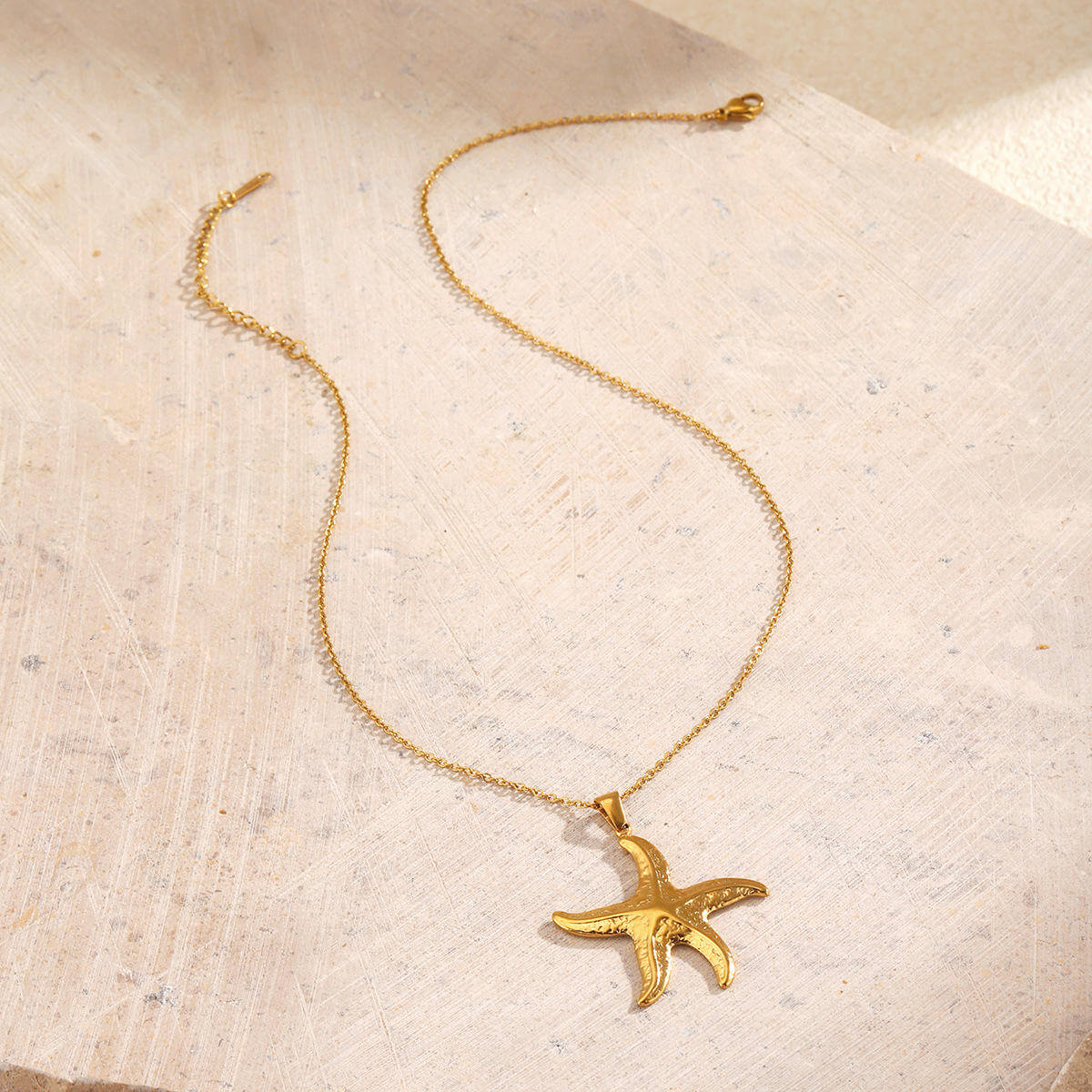 Gold Starfish Pendant Necklace on a textured beige surface