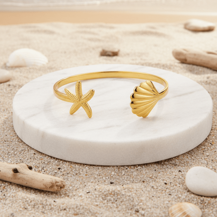 Gold Starfish & Shell Bangle Bracelet on a white stone with a beach background