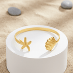 Gold starfish and shell ring on a white stand with seashells and sand in the background