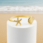Gold Starfish & Shell Bangle Bracelet with starfish and shell design on a white candle