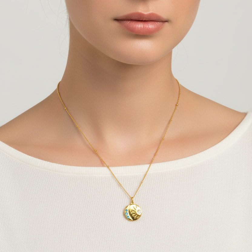A close-up of a model wearing a delicate Gold Sunburst Gemstone Necklace gold-toned pendant featuring light blue and white enamel details, paired with a white ribbed top against a light gray background.