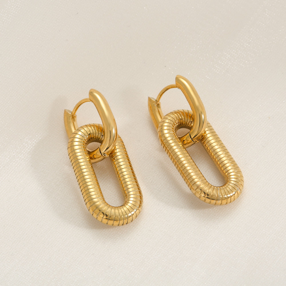 Pair of Gold Textured Oval Link Hoop Earrings on a light beige background