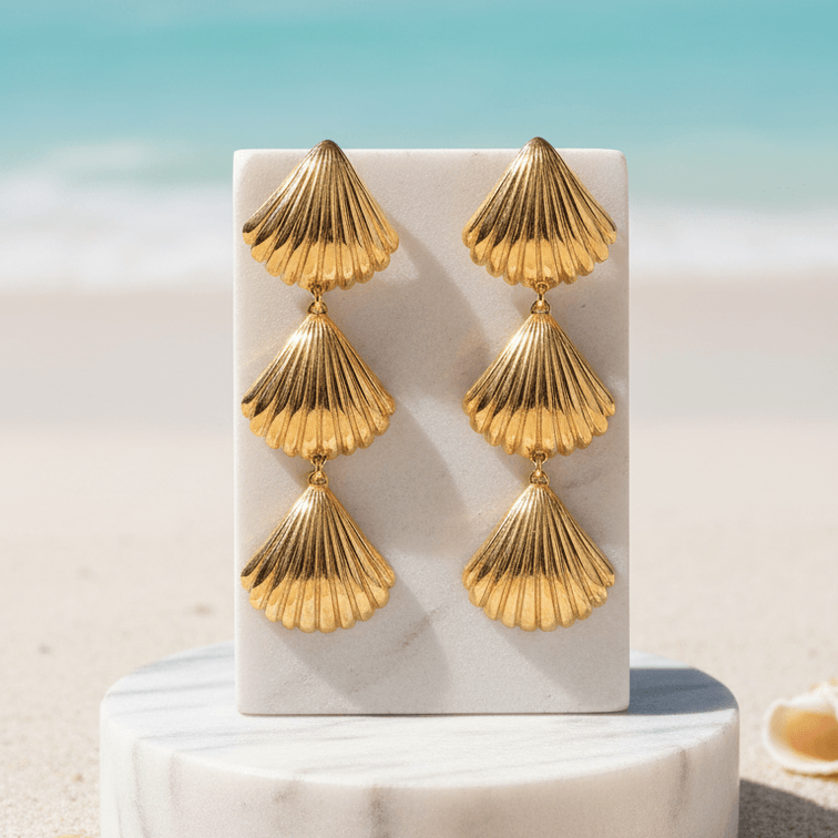 Gold Tiered Seashell Earrings on a white stand with a beach background