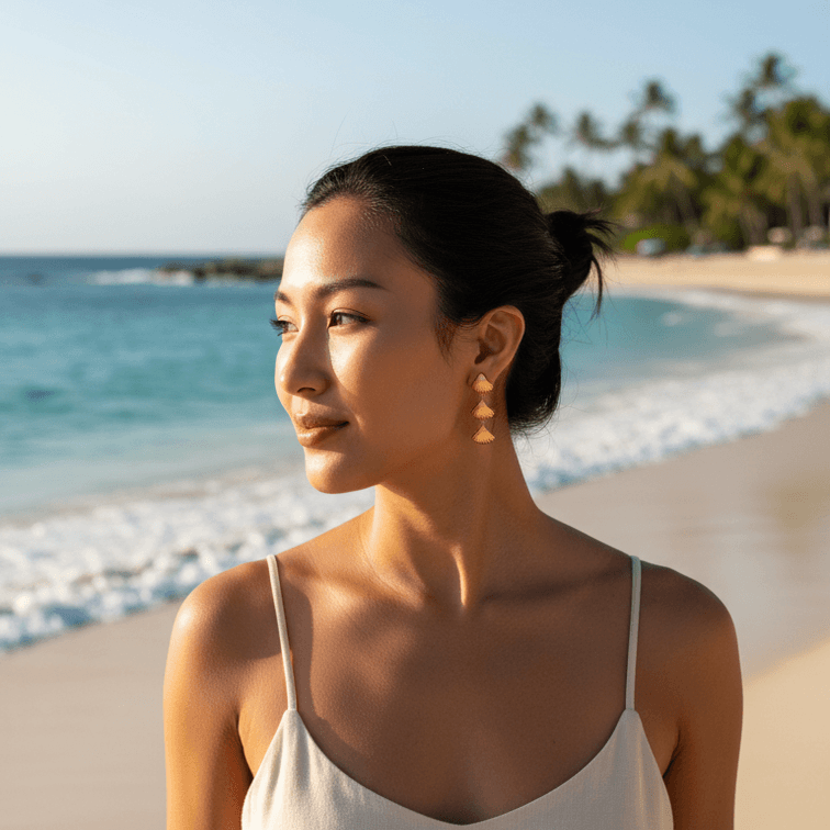 Woman in a white dress standing on a beach with palm trees in the background wearing Gold Tiered Seashell Earrings