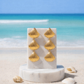 Gold Tiered Seashell Earrings on a marble stand with a beach background