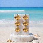 Gold Tiered Seashell Earrings on a marble stand with a beach background