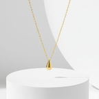 Gold Water Drop Necklace on a white pedestal with a white background
