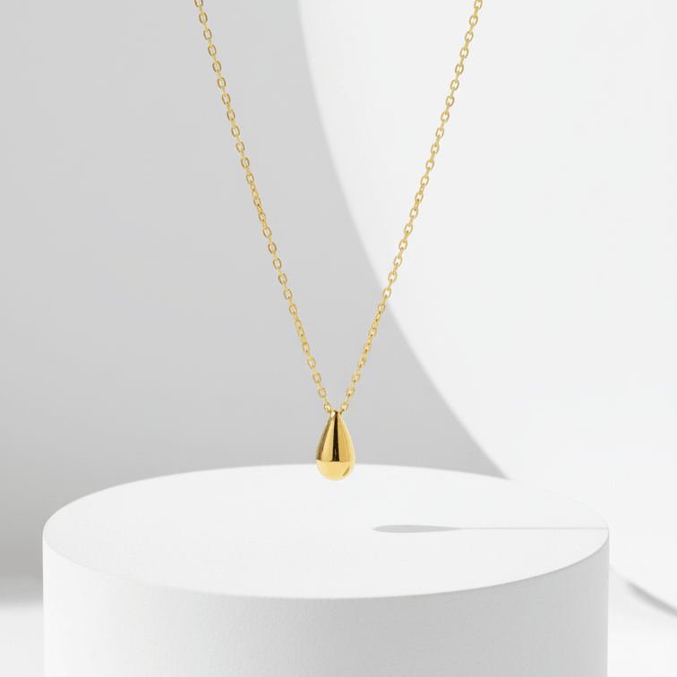 Gold Water Drop Necklace on a white pedestal with a white background