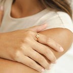 Close-up of a woman's hand wearing a Dainty Bloom Open Gold Adjustable Ring, with a blurred background.
