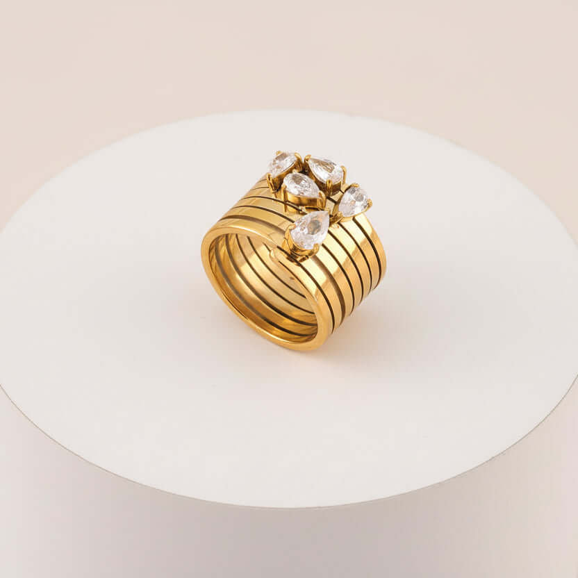 Stacked Gold Teardrop Ring featuring layered bands and clear teardrop-shaped gemstones on a white pedestal.