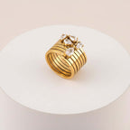 Stacked Gold Teardrop Ring featuring layered bands and clear teardrop-shaped gemstones on a white pedestal.