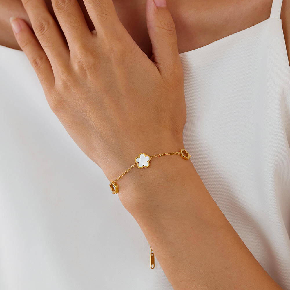 Gold bracelet with a flower-shaped charm on a wrist against a white background
