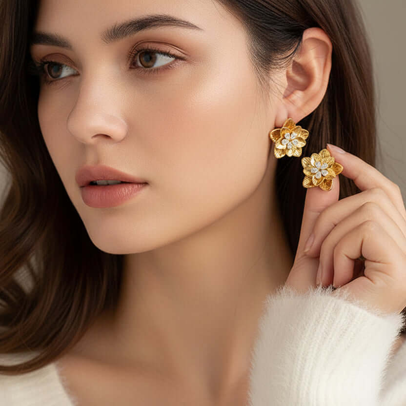 gold floral shaped stud earrings worn by a person with a neutral background