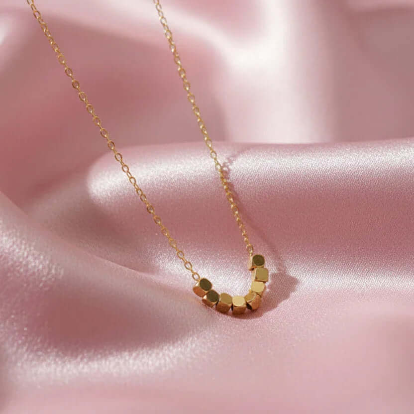 Gold hexagon bead necklace from Ceyrah on pink satin background