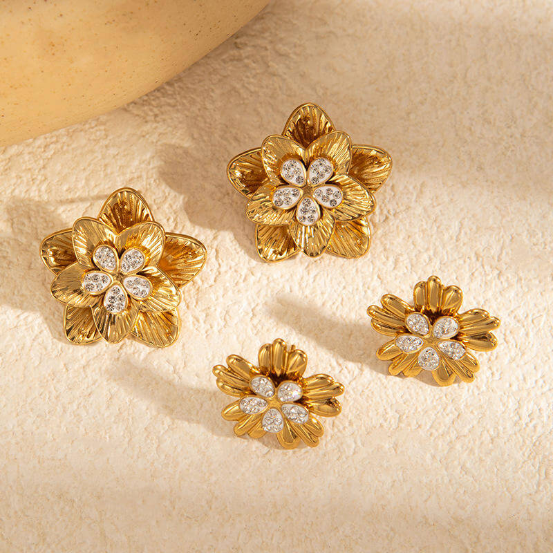 gold floral shaped stud earrings with diamond-like stones on a beige surface