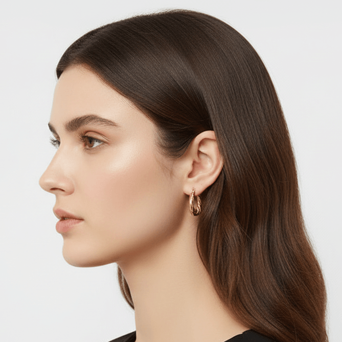 Close-up of a woman wearing Gold Twisted Rope Hoop Earrings with a plain background