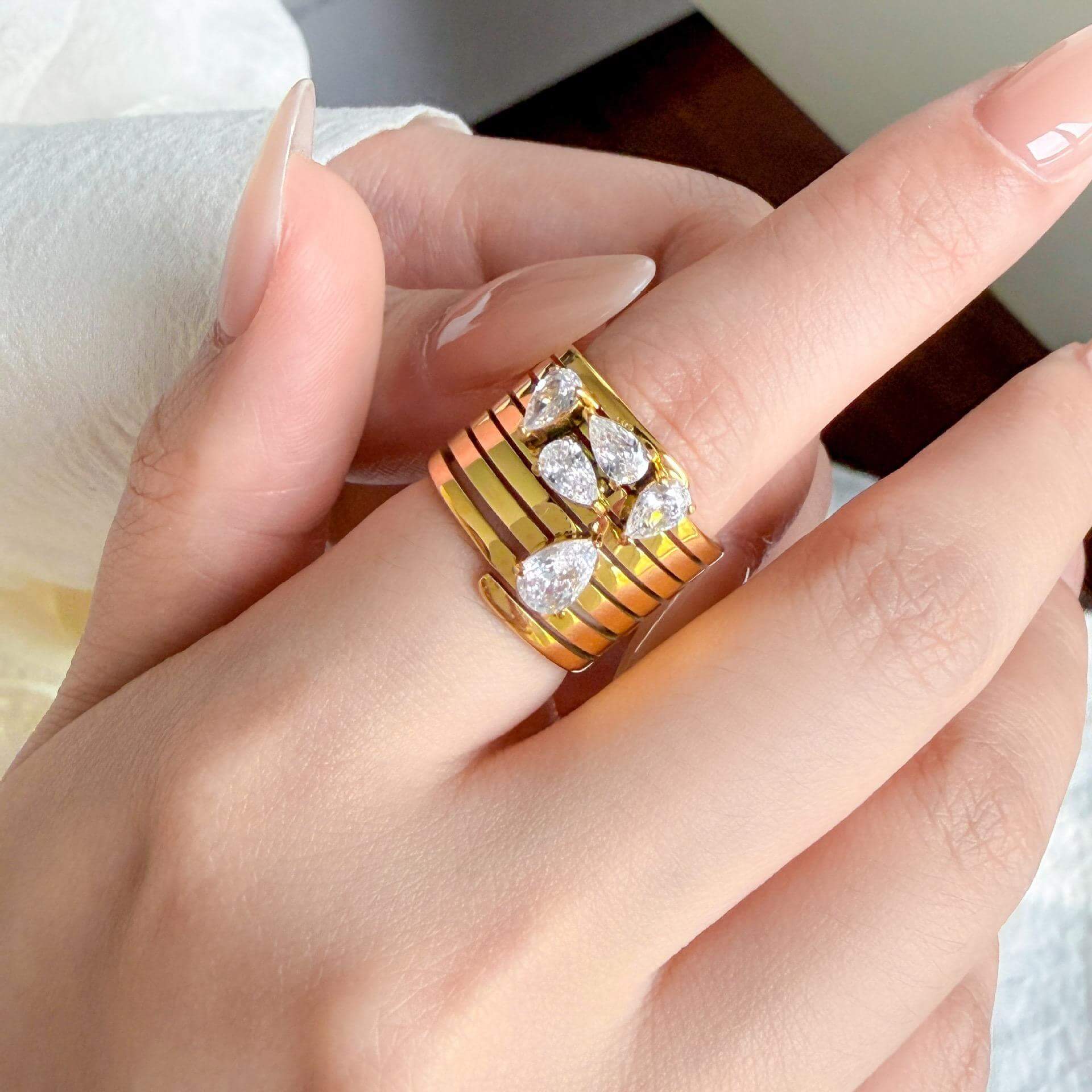 Stacked Gold Teardrop Ring worn on a hand, showcasing layered bands and clear teardrop-shaped gemstones.