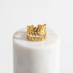 Gold Leaf & Chain Adjustable Ring displayed on a marble pedestal, showcasing its dual-motif design of a leaf and chain link.