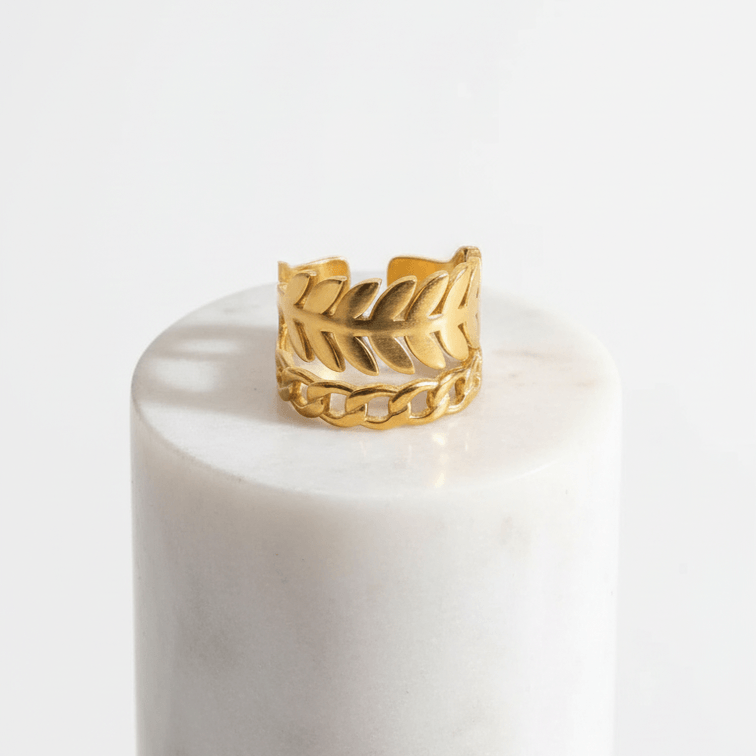 Gold Leaf & Chain Adjustable Ring displayed on a marble pedestal, showcasing its dual-motif design of a leaf and chain link.