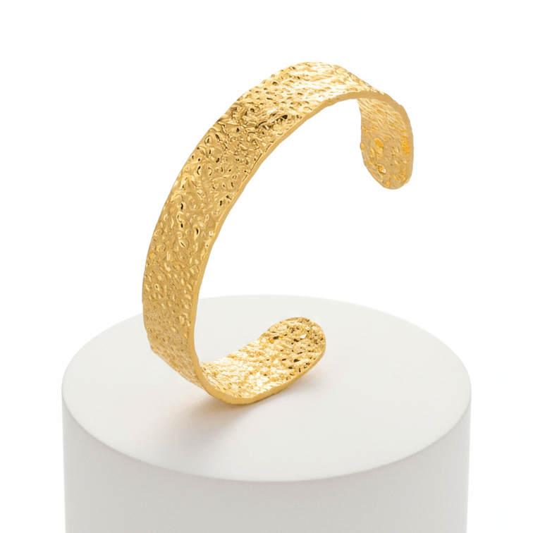 Gold textured bracelet on a white pedestal against a white background